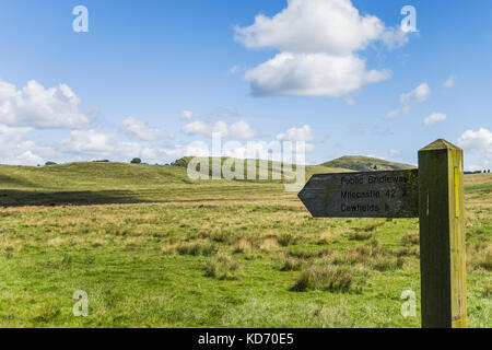 British landscape featuring Northumberland, with a public footpath sign pointing towards the Roman or Hadrian's Wall with blue sky and fluffy cloud. Stock Photo