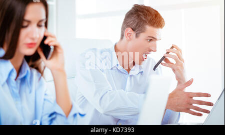 Young stressed businessman yelling on smartphone and looking at laptop. Stock Photo