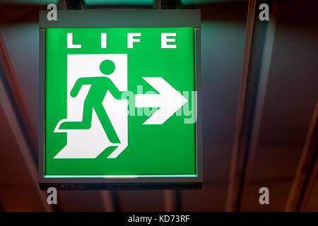 The emergency exit sign shows the direction of Life. The emergency exit board hangs on the ceiling of the building. Stock Photo