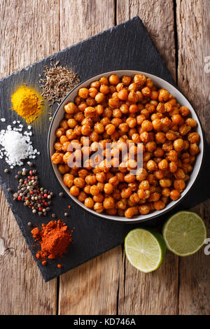 Snack of fried chickpeas with spices close-up in a bowl on the table. Vertical top view from above Stock Photo