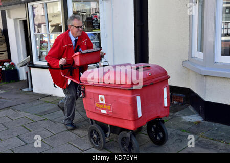 Postman pushing cart making deliveries on rounds in small English market town of Thornbury, South Gloucestershire Stock Photo
