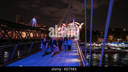 People walking along the Hungerford footbridge against the backdrop of Charing Cross at night Stock Photo
