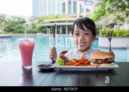 Asian Little Chinese Girl Eating Burger and French fries at Outdoor Cafe Stock Photo