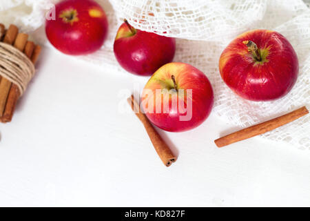 Fresh ripe red apples and cinnamon sticks on white wooden background. Stock Photo