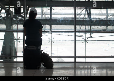 Woman traveler sitting on luggage suitcase in the airport, Silhouette with airport view Stock Photo