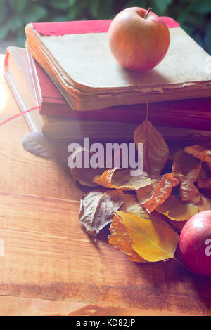 Back to school concept. Old vintage books and apple over autumn leaves in sunlight on wooden background. Stock Photo