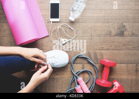 Overhead view of sport and fitness woman tying shoes with mobile devices and sport equipments on wooden floor Stock Photo