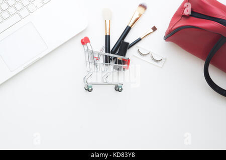 Beauty items and cosmetics in shopping cart with laptop computer on white background, Online shopping Stock Photo