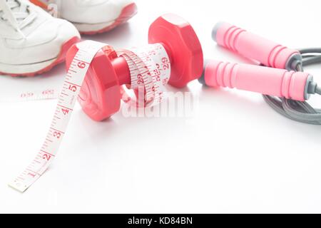 Measuring tape wrapped around red dumbbell with sport shoes and jump rope isolated on white background with copys space, Healthy lifestyle concept Stock Photo