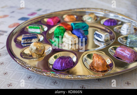 Colorfully wrapped pralines presented on golden plate or dish on table with shallow depth of field. Stock Photo