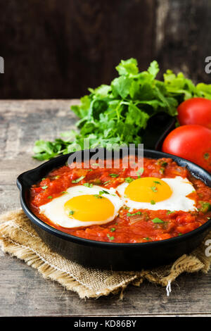 Mexican breakfast: Huevos rancheros in iron frying pan on wooden table Stock Photo