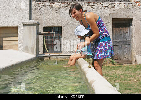 Mother holding her daughter sitting on the edge of a fresh water fountain Stock Photo