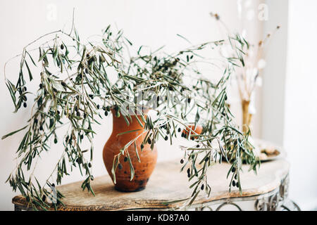 Olive Branches in a vase next to a candle on a sideboard table