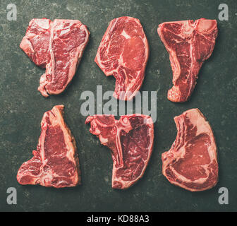 Flat-lay of fresh raw beef meat steak cuts over black stone background, top view. Porterhouse, t-bone and rib-eye steaks. Butcher' s shop or cooking m Stock Photo