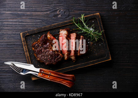 Sliced grilled meat barbecue steak Rib eye with knife and fork on burned black wooden background Stock Photo