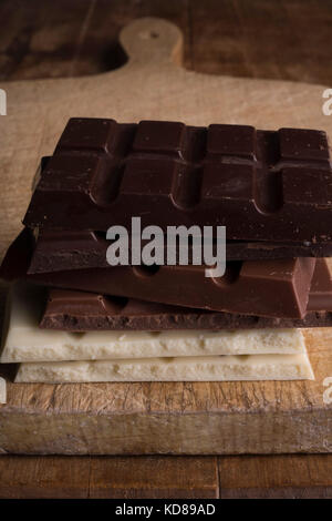 Stack of different types of chocolate on antique wooden board. Stock Photo