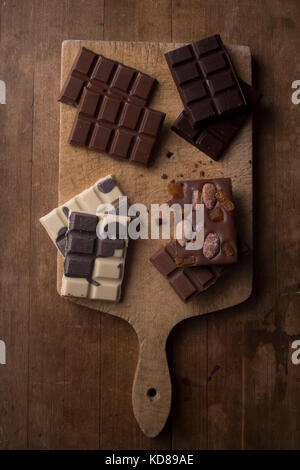 Multiple types of chocolate laid out on a rustic wooden cutting board. Stock Photo