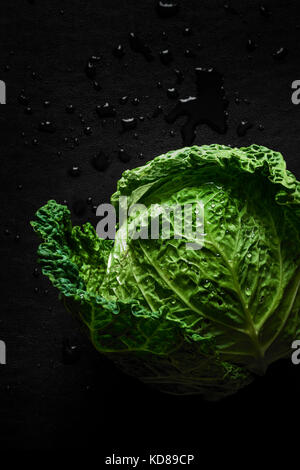A fresh picked head of vibrant green cabbage with water droplets on a dark surface. Stock Photo