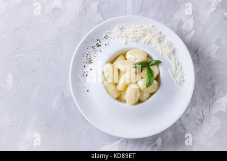 White plate of hot creamy potato gnocchi served with black pepper, grated parmesan and fresh basil over gray concrete background. Flat lay with space Stock Photo