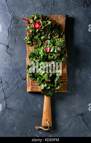 Cutting fresh chard mangold salad on wooden chopping board over black texture background. Top view with space Stock Photo