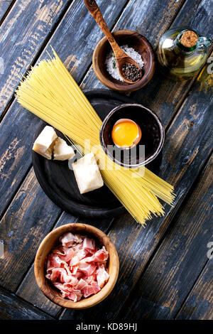 Ingredients for traditional italian pasta alla carbonara. Uncooked spaghetti, pancetta bacon, parmesan cheese, egg yolk, salt, pepper in olive wood bo Stock Photo