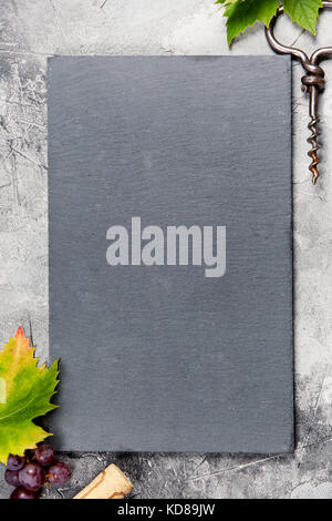 Top view of a blank chalk board for a wine list or menu with an old cork screw and grape leaf on gray concrete background with space for text.  A vert Stock Photo