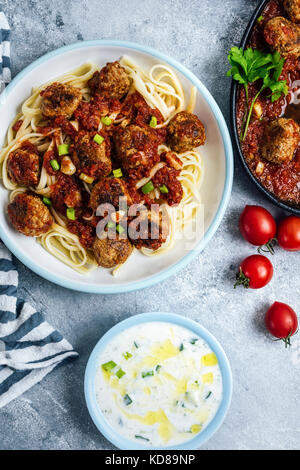 Meatballs with tomato sauce served on pasta photographed from top view. Yogurt and cucumber dip in a small bowl and tomatoes accompany. Stock Photo