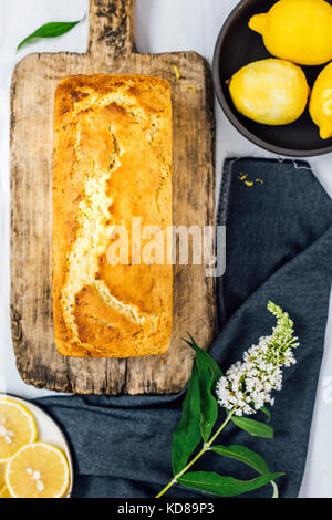 Lemon zucchini bread on a wooden board is photographed from top view. Lemons, lemon slices and a flower accompany this. Stock Photo