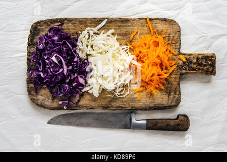 Shredded white cabbage, purple cabbage and carrot ready on a wooden board for coleslaw photographed from top view. Stock Photo