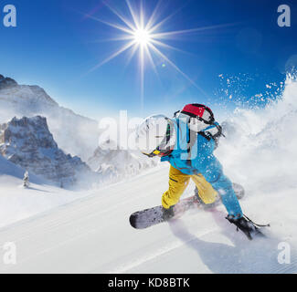 Young man snowboarder running down the slope in Alpine mountains. Winter sport and recreation, leasure outdoor activities. Stock Photo