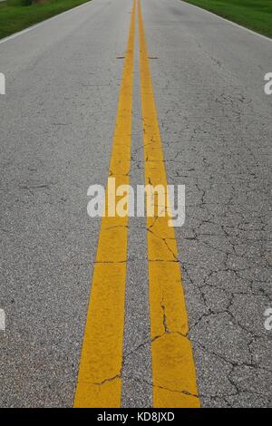 Double yellow centre lines on a cracked road surface in the USA Stock Photo