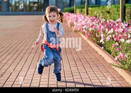 funny little girl jumping for joy.little girl in denim jumpsuit. Stock Photo