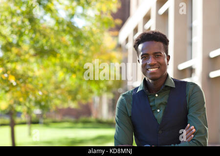 A handsome young black male student smiles standing on college campus Stock Photo