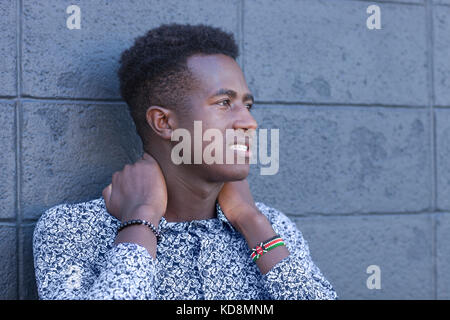 Handsome young black man stands in front of gray block wall with hands on neck Stock Photo