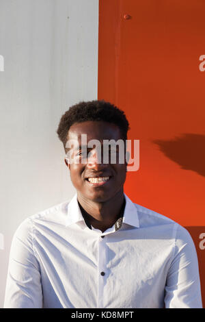 Handsome young black man in white shirt smiling in front of orange and white divided background Stock Photo