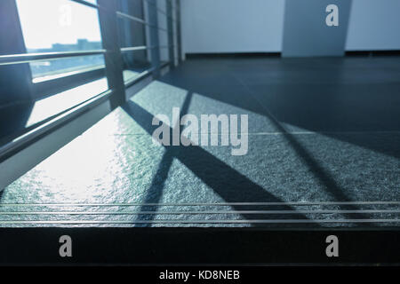 Railing as shadow in backlight on floor tiles on ground of a office building Stock Photo