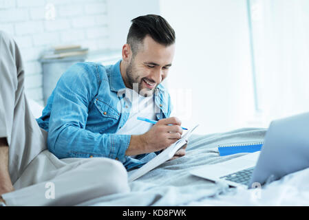 Radiant male student preparing home assignment in bed Stock Photo