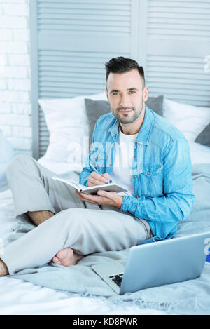 Kind young man looking into camera while taking notes Stock Photo