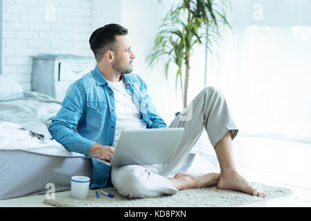 Thoughtful young man dreaming while working on laptop Stock Photo