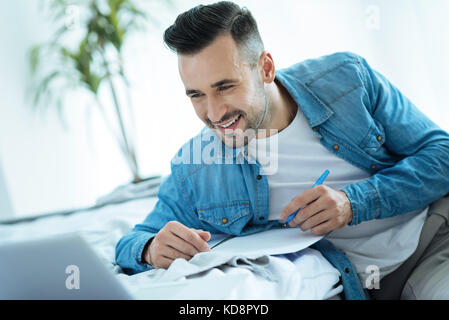 Smiling man looking at laptop while taking notes Stock Photo