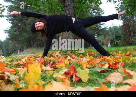 beautiful flexible woman made yoga practice on green grass covered bright autumn foliage Stock Photo