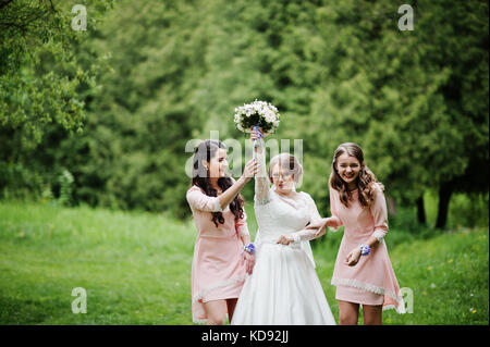 Attractive bride posing and having fun with two her bridesmaids in the park on a sunny spring wedding day. Stock Photo