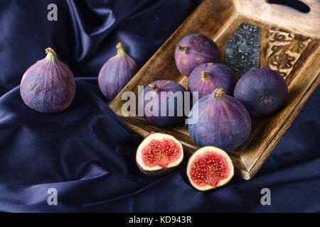 Fresh ripe violet figs in wooden bowl on purple backdrop Stock Photo