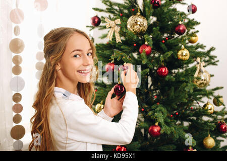 happy teenage girl decorating christmas tree at home
