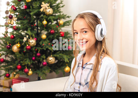 beautiful happy teenage girl in headphones listening music and smiling at camera at christmas eve Stock Photo