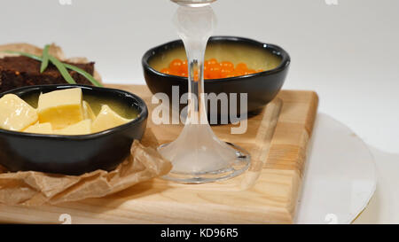 Diced butter, caviar, black bread. Bowl of red caviar with spoon served with sliced bread, butter and herbs on white background. Wholegrain bread, butter and red caviar, white background Stock Photo