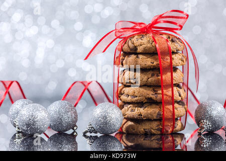 Stack of chocolate chip cookies with Christmas ornaments reflection on the glass table over silver background Stock Photo