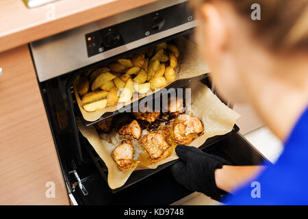 woman preparing potatoes and chicken meat in oven at home kitchen Stock Photo