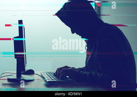 Hooded computer hacker working on desktop PC computer. P2P and piracy, computer virus and trojans, phishing, malware and ransomware concept with glitc Stock Photo