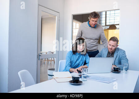 Focused office coworkers talking together while using a laptop  Stock Photo